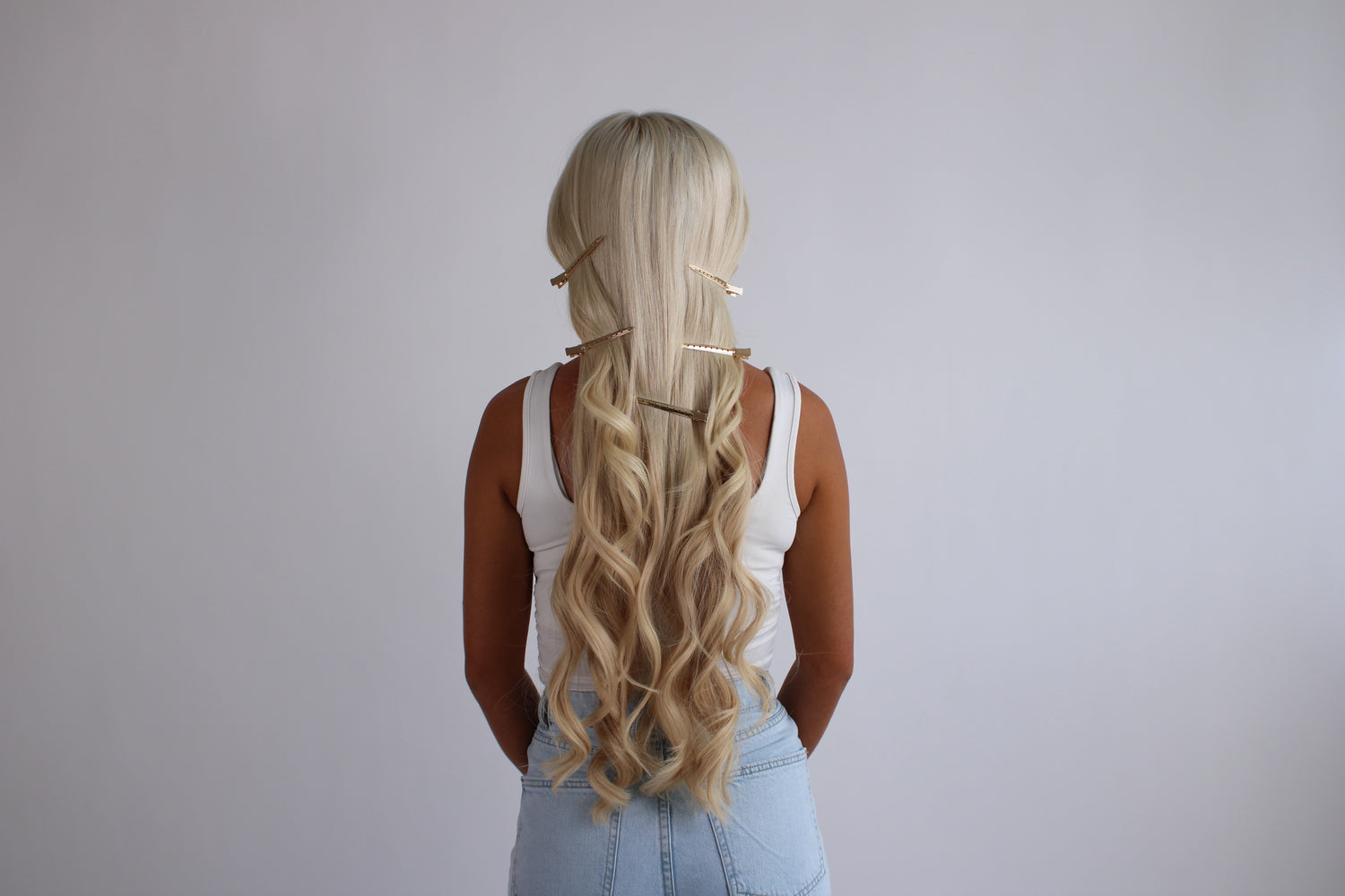 Person with long blonde hair styled in a loose waves against a plain background