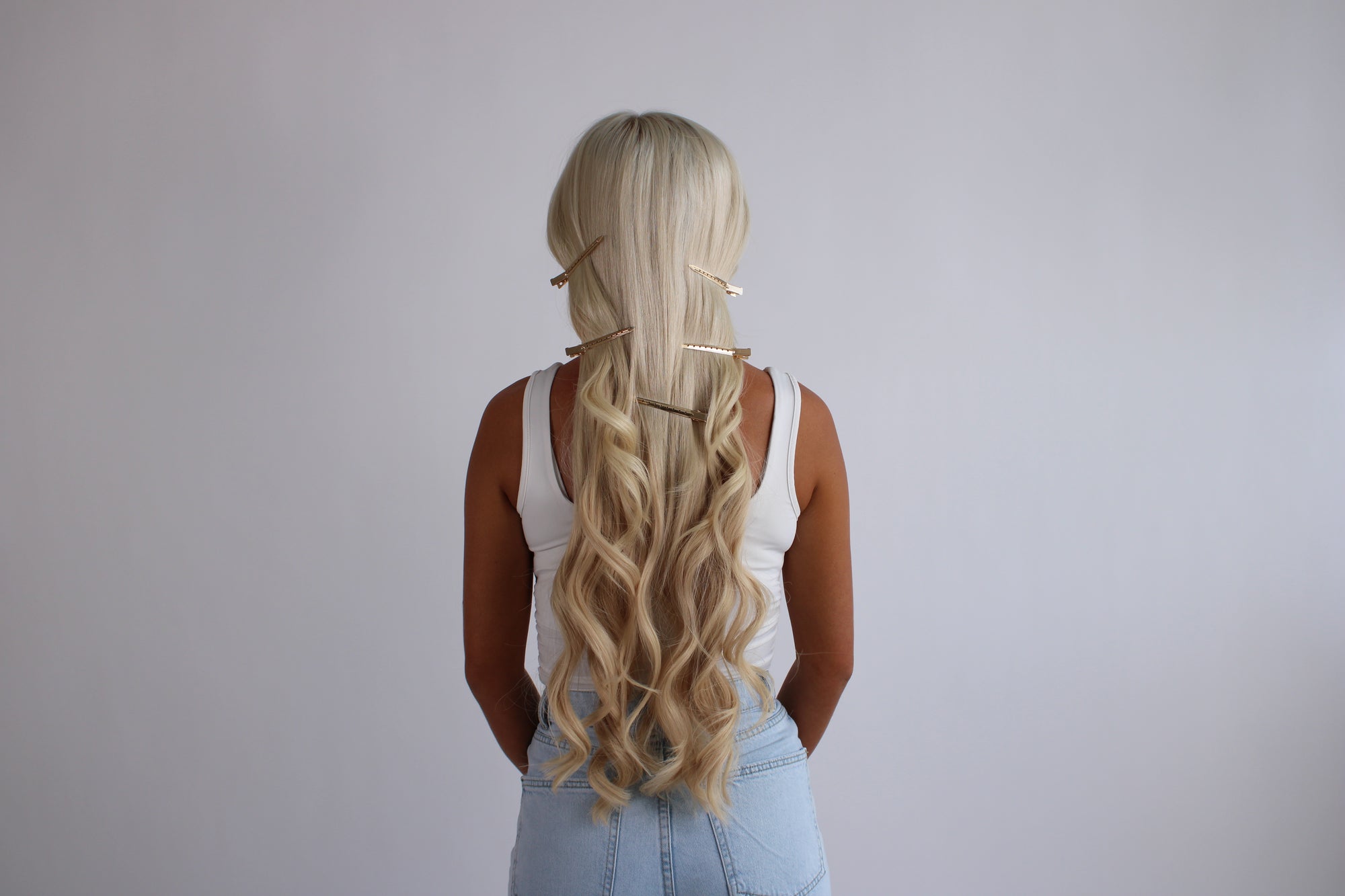Person with long blonde hair styled in a loose waves against a plain background